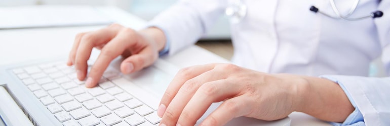 Mãos de um profissional da saúde sobre teclado de computador ilustrando a consulta a agenda médica.