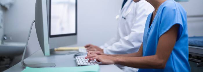 Faturamento TISS ilustrado com a foto de profissionais da saúde utilizando computadores para preencher formulários eletrônicos.