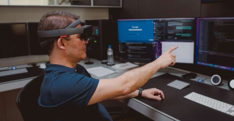 ProDoctor 30 anos - CEO aponta em direção ao futuro, ele usa camisa azul marinho, está numa sala com computadores e usa um óculos de realidade aumentada