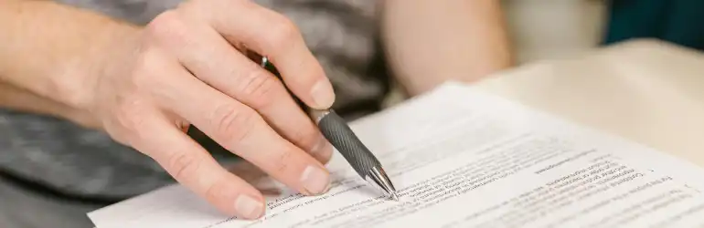 Atualizações Revalida Medicina: pessoa escrevendo em um documento com caneta. A imagem demonstra a importância da documentação burocrática, como a obrigatoriedade da carta de habilitação prévia