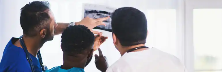 Etapas do Revalida medicina: três profissionais de saúde analisando um raio-X, destacando a importância da colaboração em diagnósticos médicos e cuidados ao paciente.