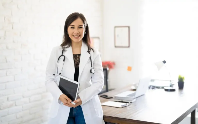 Médica sorridente em seu consultório, segurando um tablet, com um estetoscópio no pescoço. Ambientes de saúde e bem-estar.