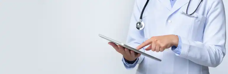 Médico usando tablet, vestindo jaleco branco e com estetoscópio, simbolizando a responsabilidade médica através da documentação clínica adequada.