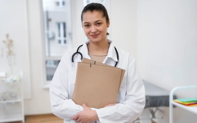 Médica sorridente com estetoscópio ao redor do pescoço segurando pastas na frente de uma clínica, promovendo medicina baseada em evidências.