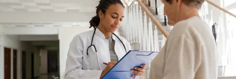 Médica olha para uma prancheta e avalia a medicina baseada em evidências enquanto atende uma paciente idosa.