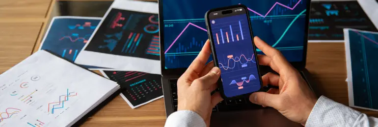 Análise de dados financeiros com gráficos, computadores e um smartphone mostrando tendências de mercado, essencial para estratégias de investimento.