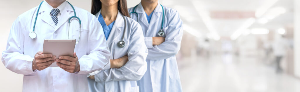 Três profissionais de saúde (dois médicos e uma médica) com estetoscópios e jalecos brancos, sendo que um deles segura um tablet, ilustrando como a tecnologia na saúde potencializa o cuidado e reforça a importância do atendimento humanizado na saúde.