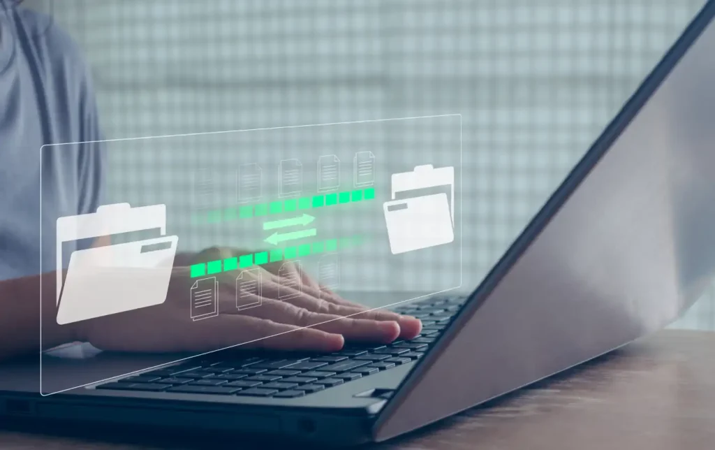 Pessoa utilizando notebook em ambiente digital, com ícones de pastas e documentos holográficos na tela, representando organização e troca de arquivos de banco de dados.